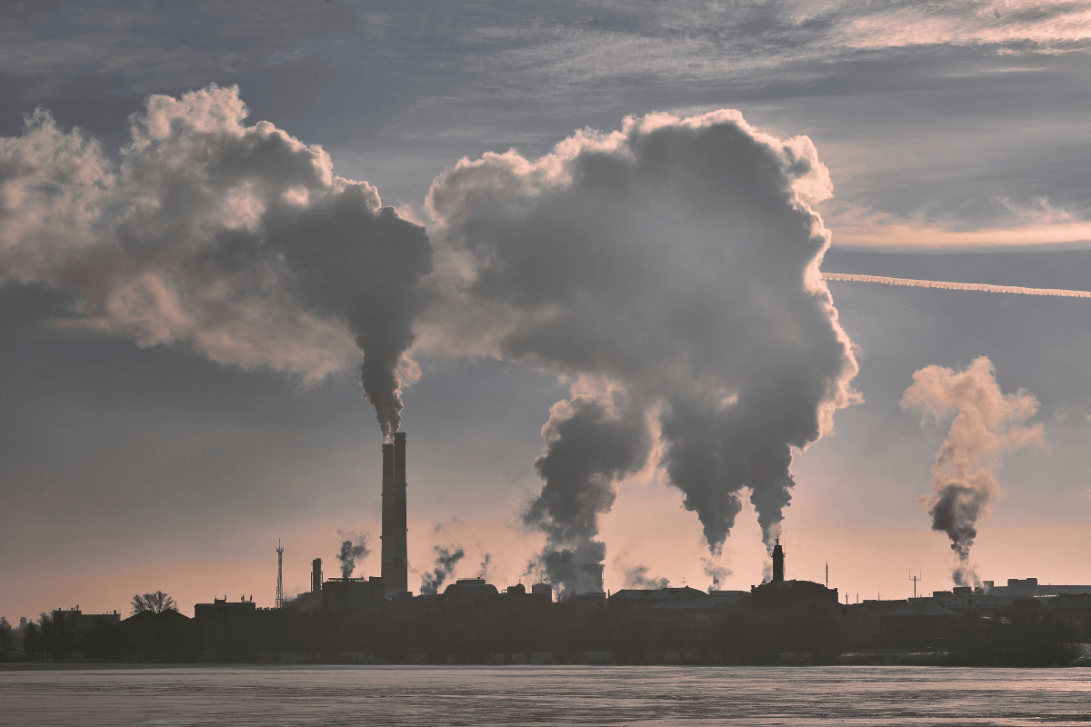 A factory with smoke stacks emitting smoke into the sky near a body of water.