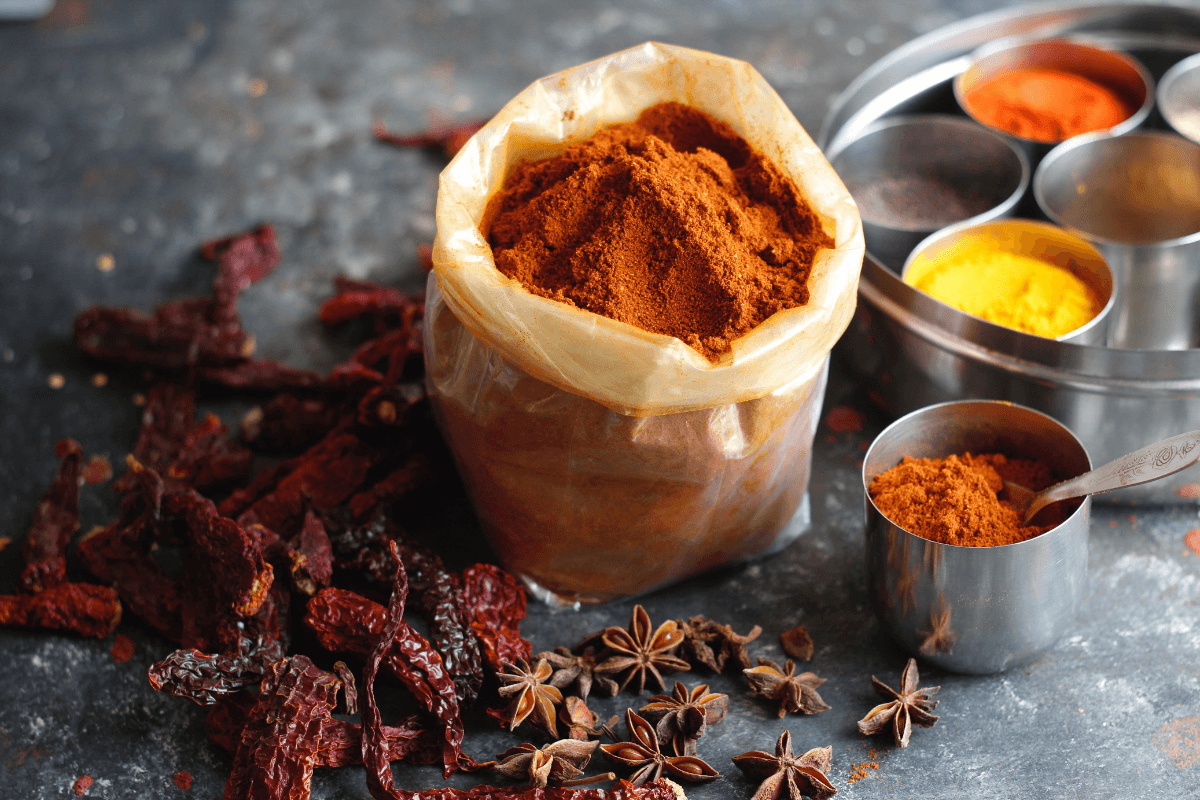 A bag of red chili powder and other spices on a dark grey countertop turmeric.