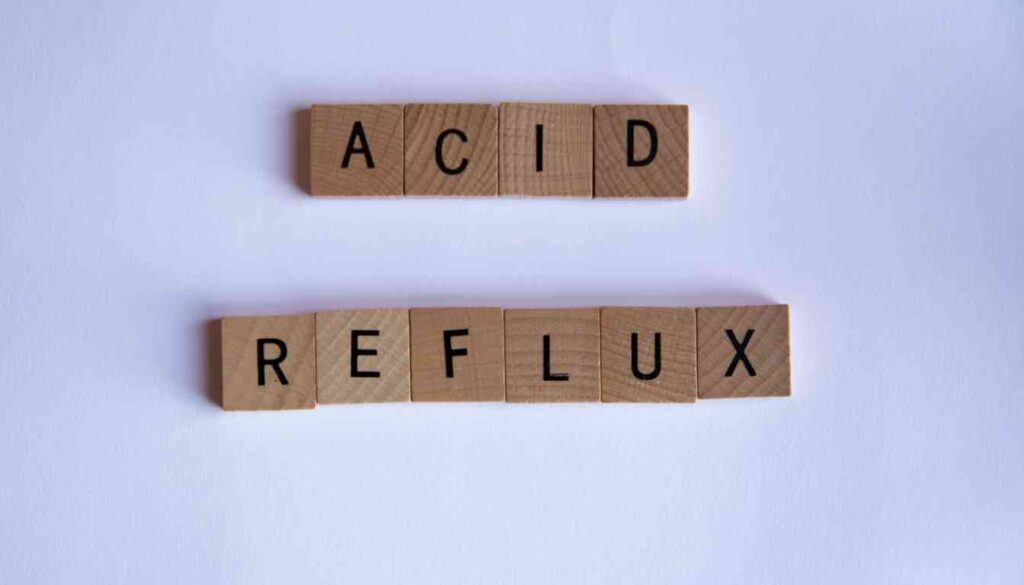 Wooden letter tiles spelling "ACID" on the top row and "REFLUX" on the bottom row against a white background.