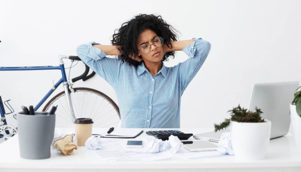 Person stretching at a cluttered desk with a bicycle in the background.