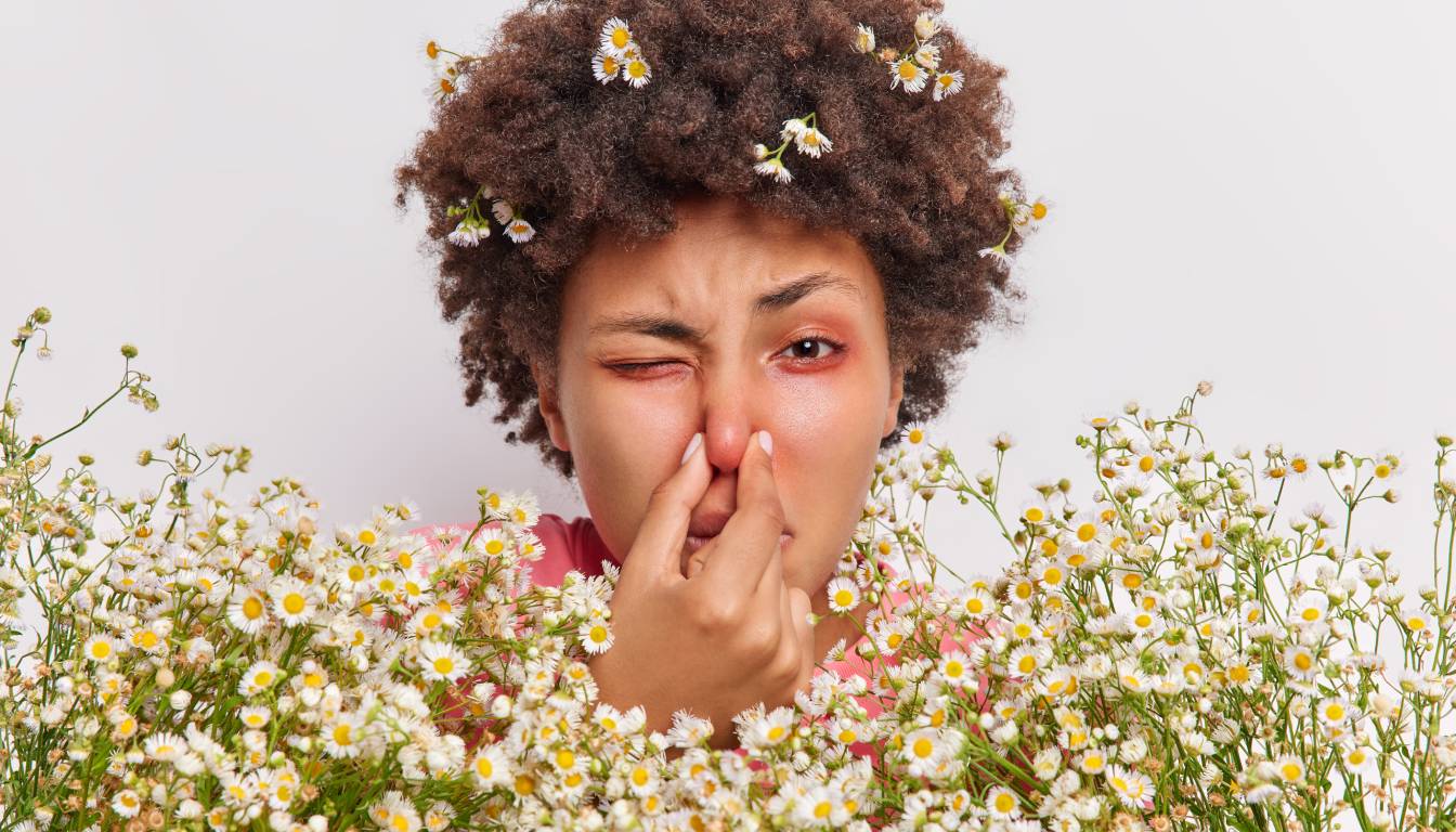 A person with curly hair adorned with small white and yellow flowers, surrounded by a dense cluster of similar flowers.