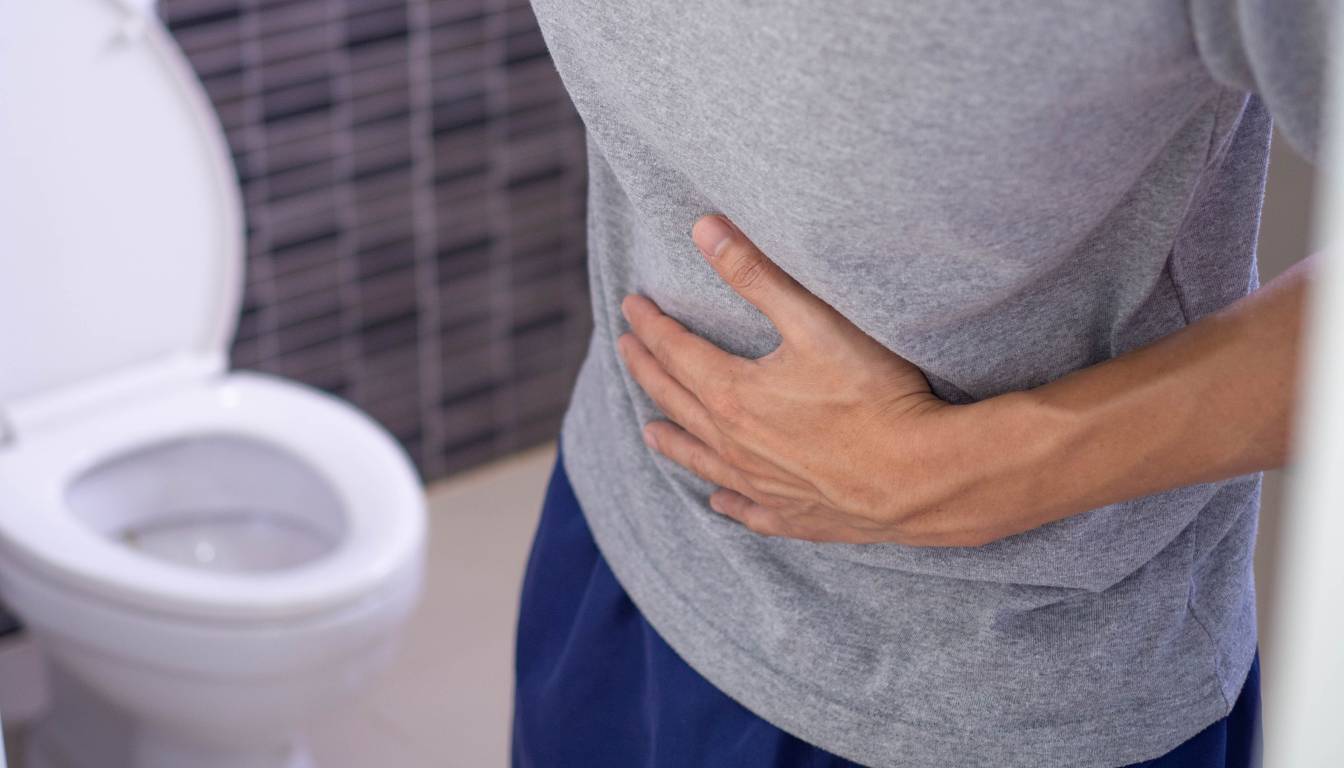 A person holding their stomach in pain while standing next to a toilet