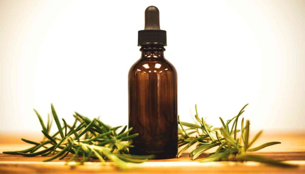 A dark glass bottle with dropper surrounded by fresh rosemary sprigs on a wooden surface.