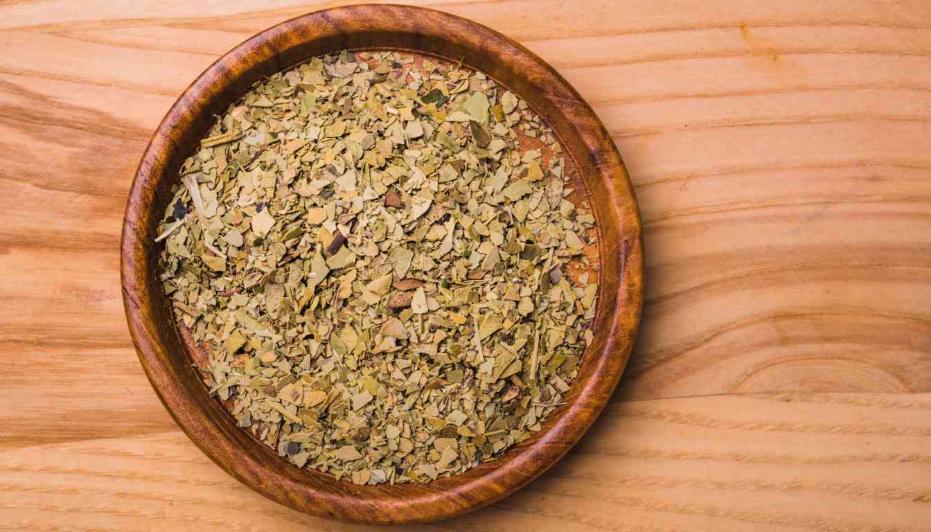 A wooden bowl filled with dried oregano leaves on a wooden surface.