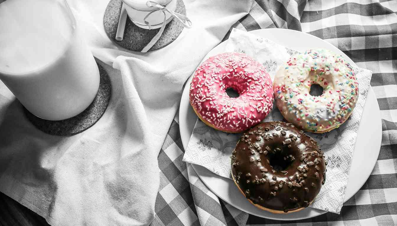 Three decorated donuts on a white plate, with a glass of milk on a checkered napkin.