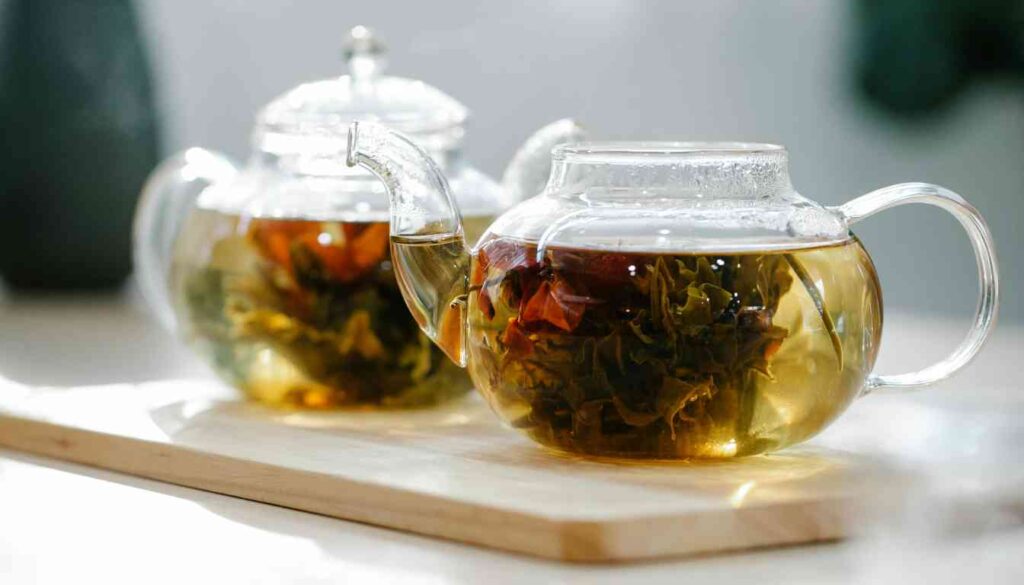 Two clear glass teapots with steeping tea leaves on a wooden board, suggesting a natural remedy for acid reflux.