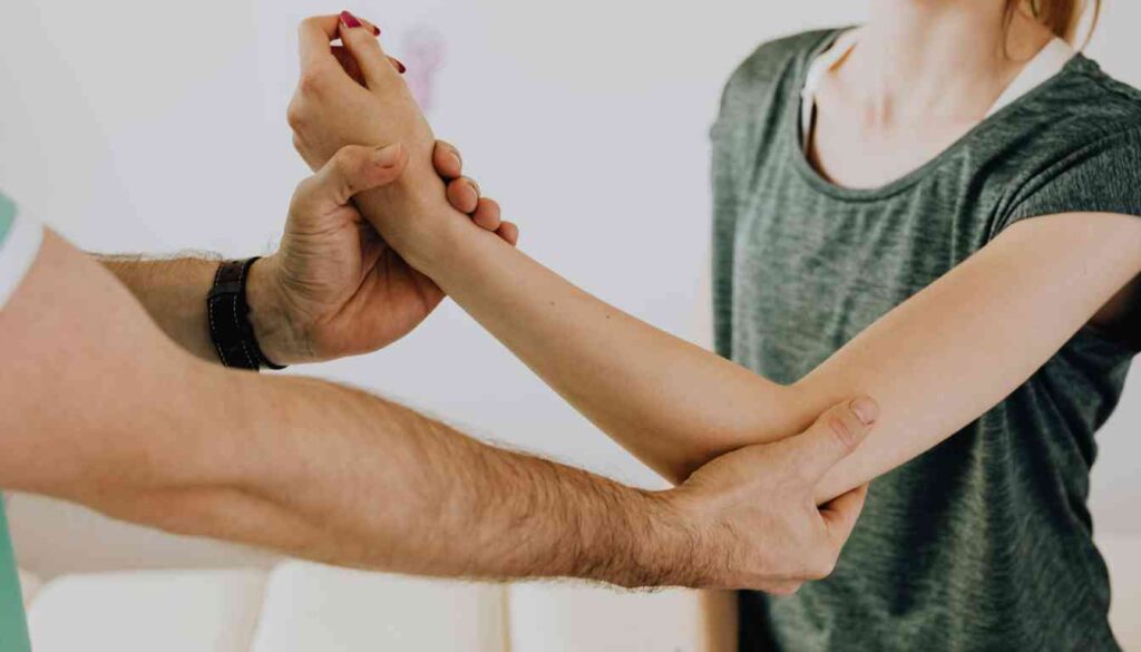 A person in a green shirt is holding and examining another person's arm, focusing on the elbow joint.