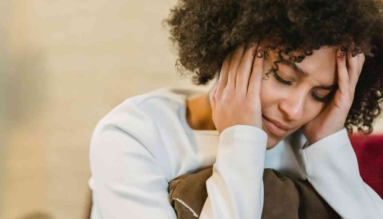 An individual with curly hair is seen from behind, resting their head in their hand, suggesting a state of discomfort which could be indicative of a headache.