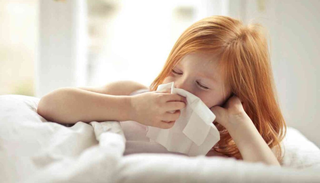 A person with red hair lying in bed, holding a tissue to their nose.