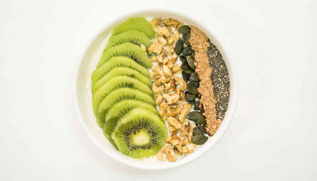 A bowl of yogurt topped with sliced kiwi, granola, pumpkin seeds, chia seeds, and flaxseed powder.