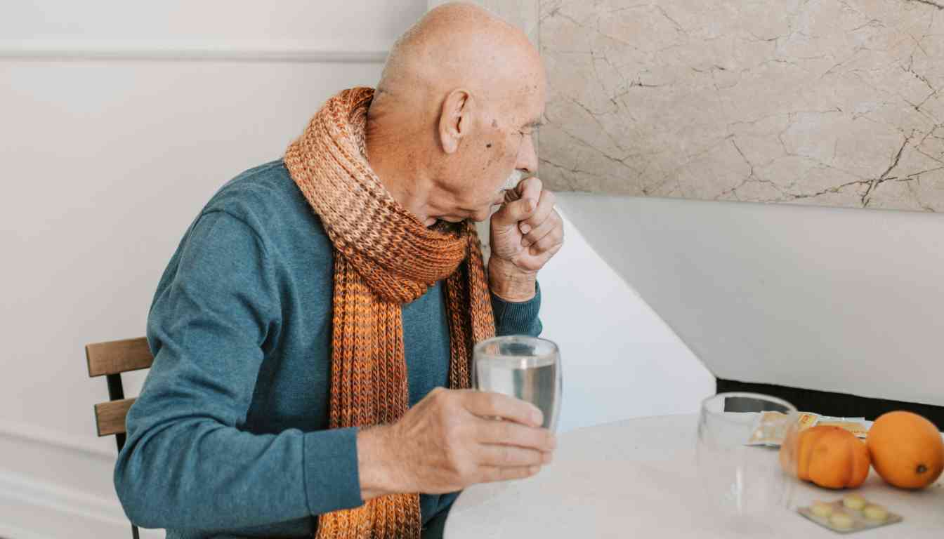 Person in blue sweater and orange scarf holding a glass with water, with oranges and medications on the table.