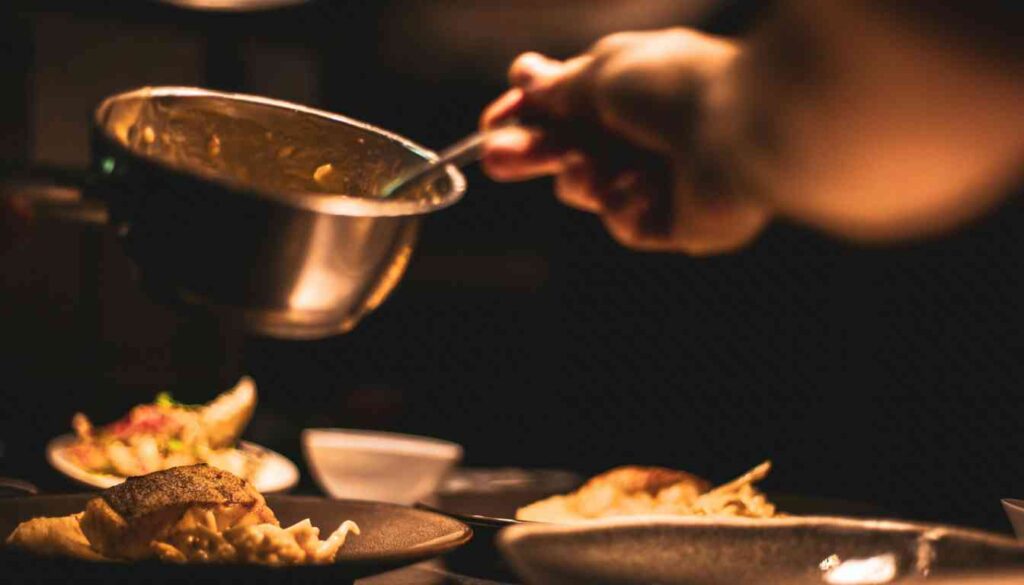 A person holding a pot of Pepperidge Farm dressing in one hand and a spoon in the other, adding dressing to plates on a table.