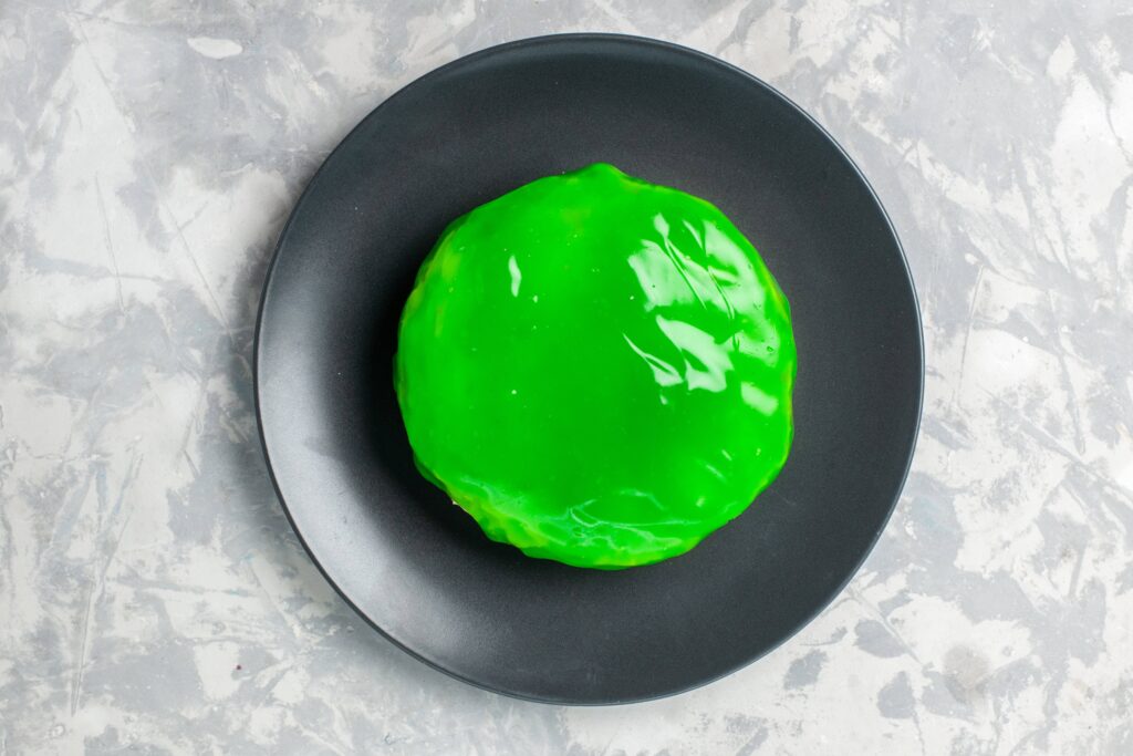 A round, green jelly dessert on a black plate, placed on a gray marbled surface.