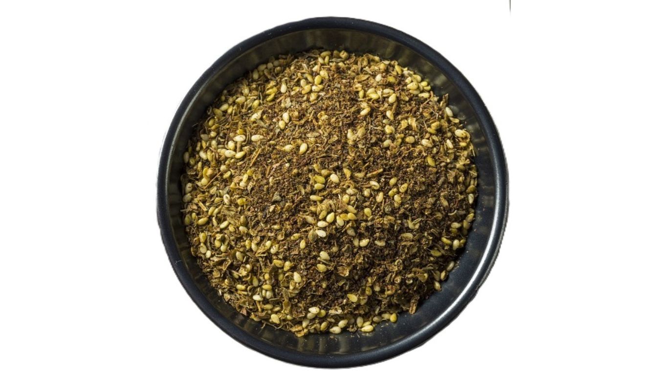 A bowl filled with a mixture of dried herbs and seeds, known as Zaatar, a Middle Eastern spice blend.