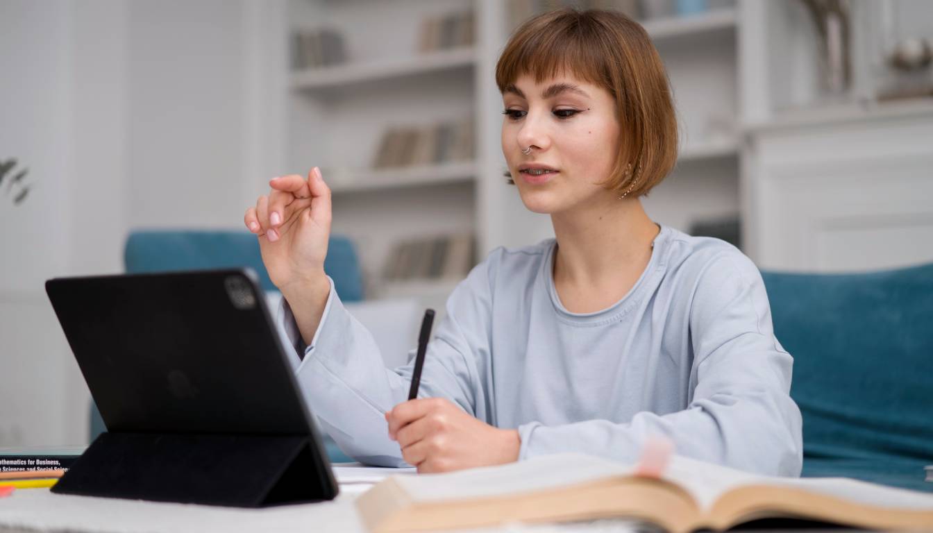 A person sitting at a desk with a tablet and an open book, appearing to study.