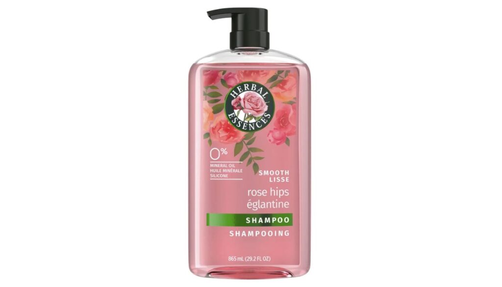 A clear bottle of Herbal Essences Rose Hips Shampoo with pink liquid, black pump, and floral graphics on the label.
