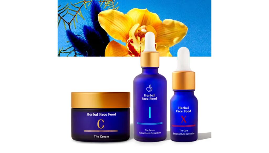 collection of Herbal Face Food skincare products, including a cream and two serums, displayed against a vibrant background featuring a yellow flower and blue feathers.