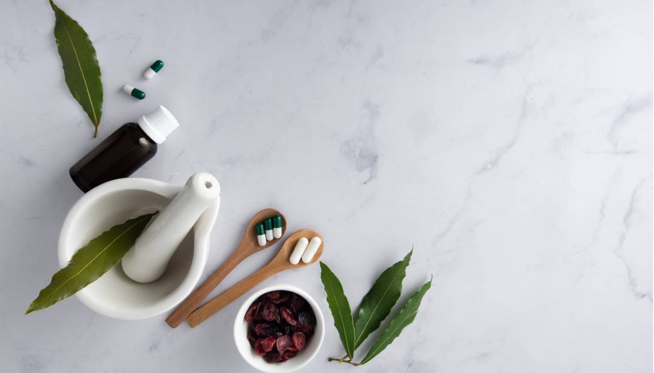 A flat lay of herbal and synthetic remedies, including a mortar and pestle with a bay leaf, a bottle of medicine, capsules, and dried berries.