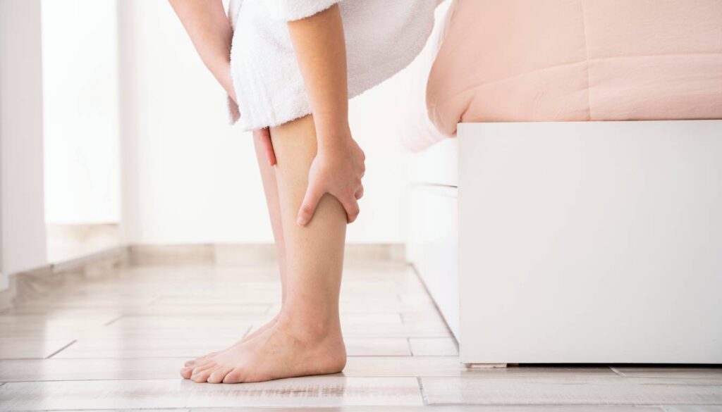 A person in a white robe holding their swollen leg, indicating discomfort from edema.