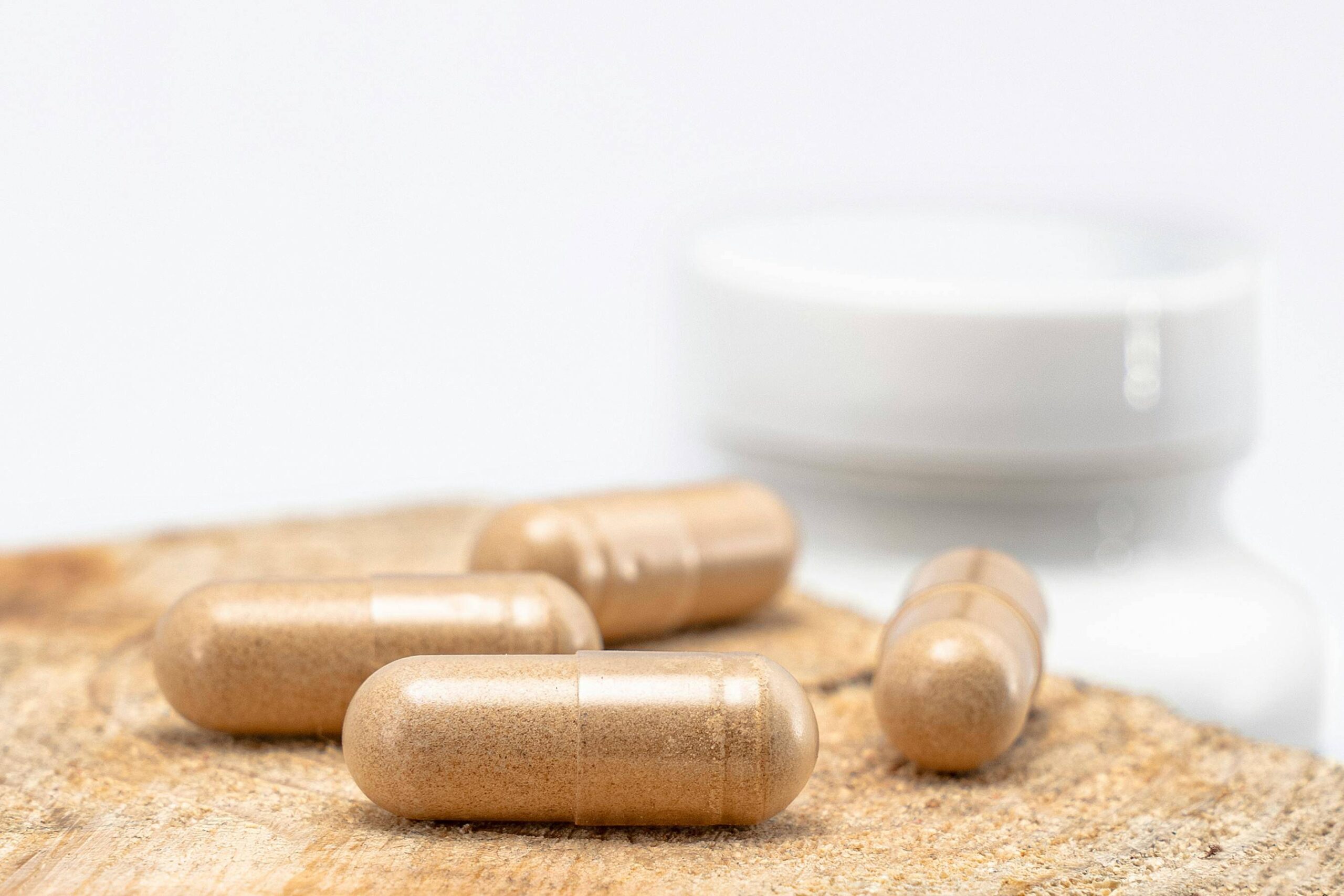 Close-up of herbal supplement capsules on a wooden surface with a white bottle in the background.