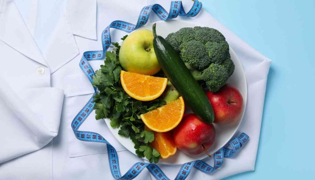 A plate filled with fresh fruits and vegetables, including apples, oranges, broccoli, cucumber, and leafy greens, placed on a white lab coat with a blue measuring tape draped around it.