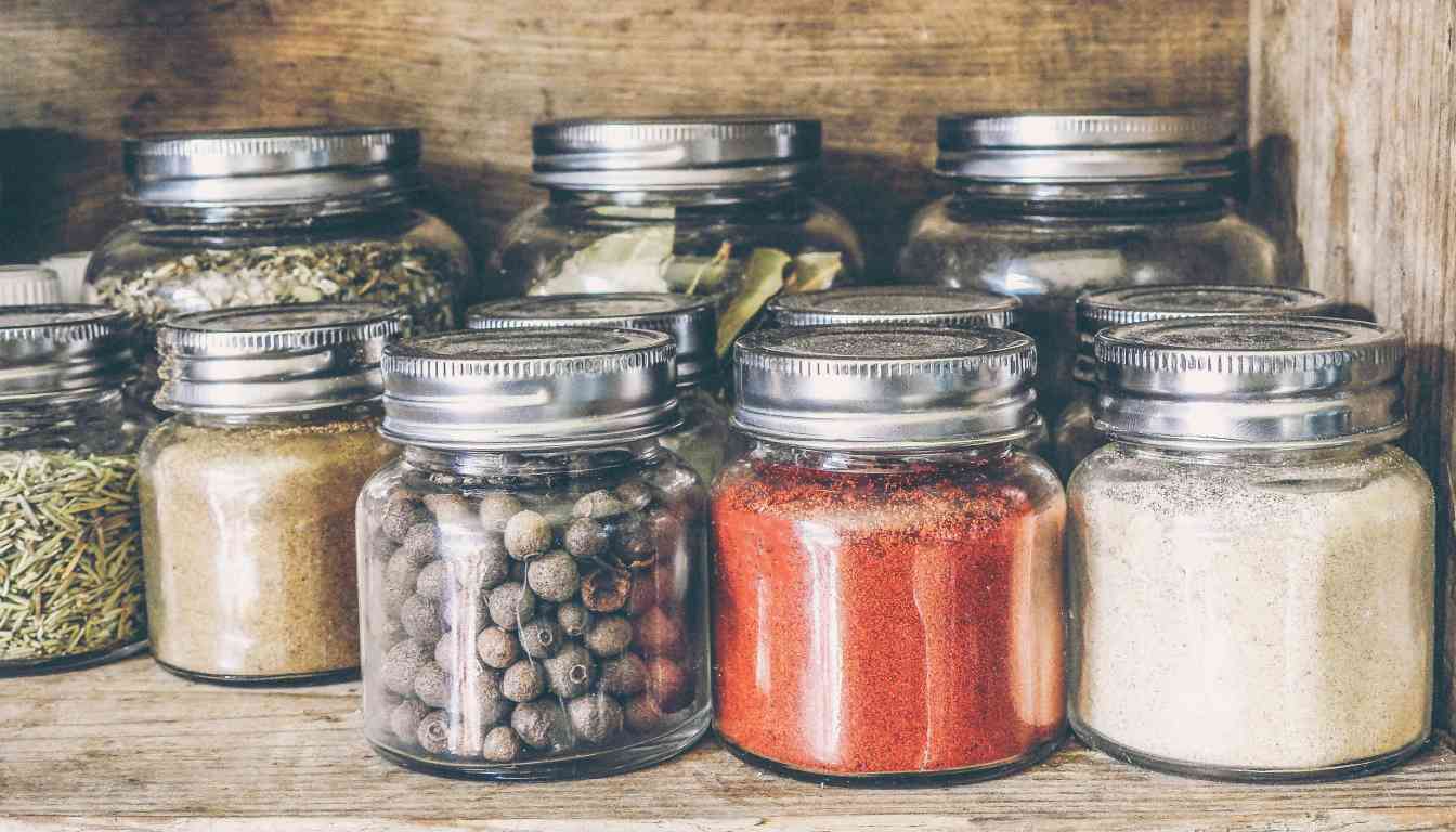 A variety of herb jars neatly arranged on a wooden shelf, containing different spices and herbs like rosemary, peppercorns, paprika, and garlic powder.