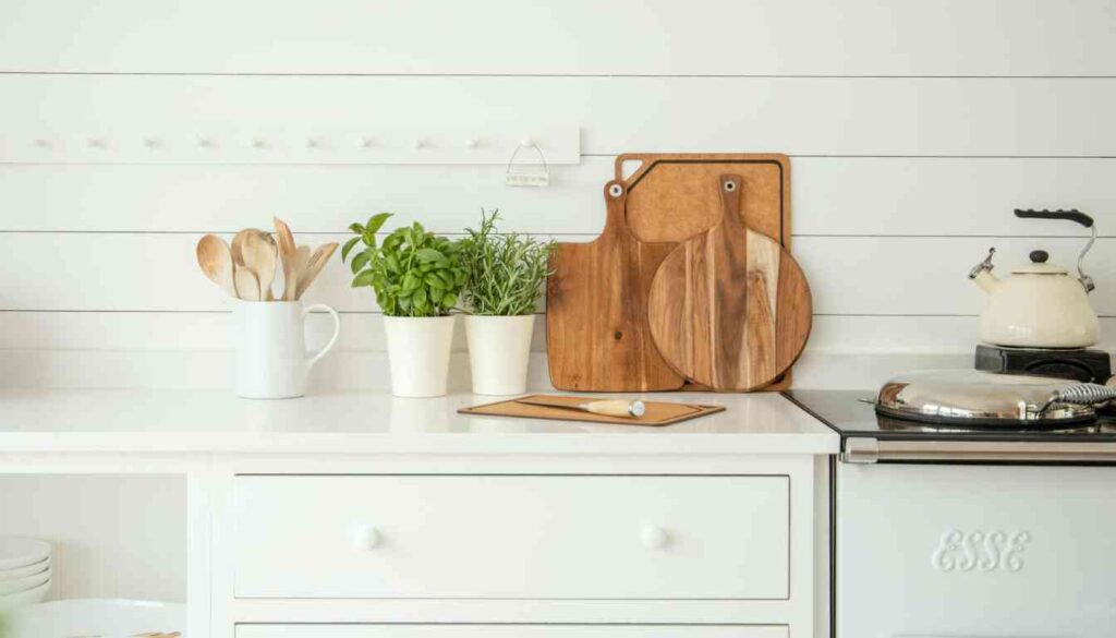 A modern kitchen counter featuring a variety of herbs growing in white pots, wooden cutting boards, and cooking utensils, illustrating the concept of ‘Growing Herbs in Kitchen’.