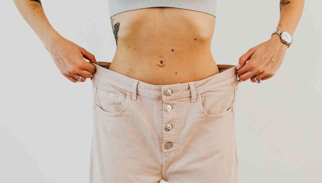 A person holding open a pair of oversized pants at the waist, demonstrating significant weight loss.