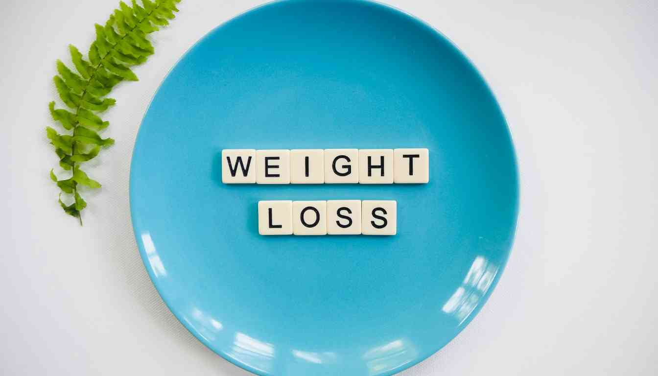 A blue plate with the words “WEIGHT LOSS” spelled out in block letters, accompanied by a green fern leaf on a white background.