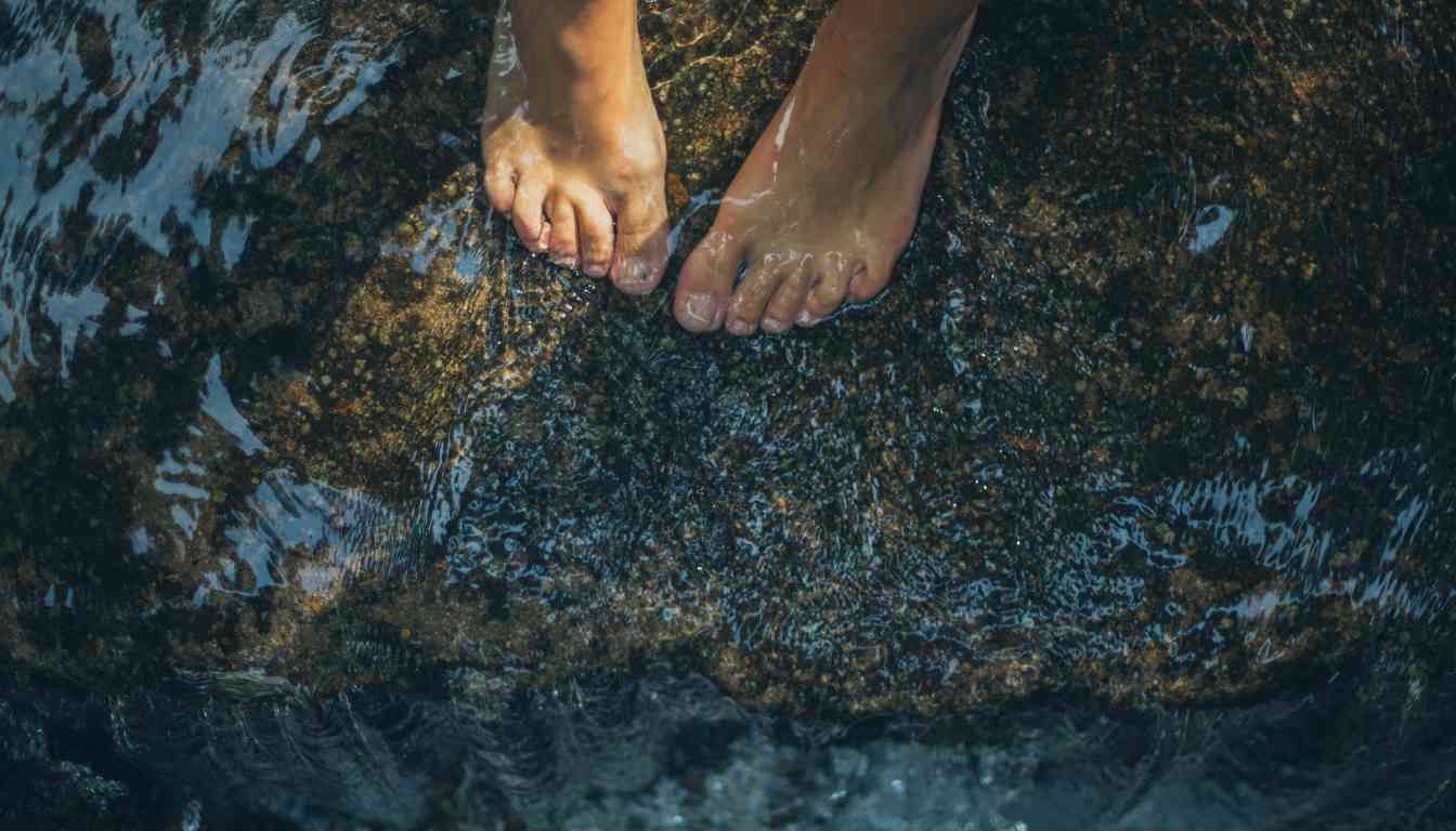 Close-up of two feet standing on a wet rock partially submerged in water.