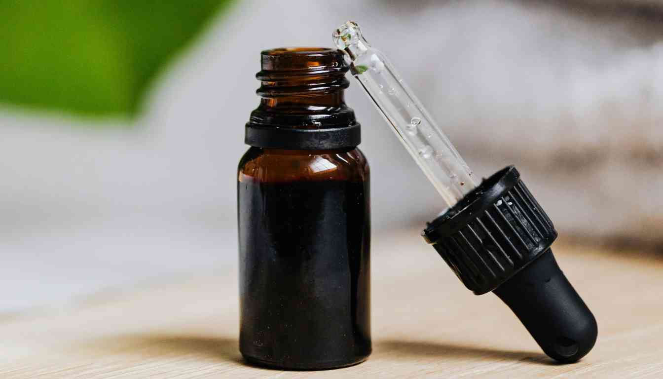 A small amber glass bottle with a black dropper cap, partially filled with a dark liquid, labeled as skullcap tincture. The dropper is resting against the bottle, with a few drops of liquid visible inside the dropper.