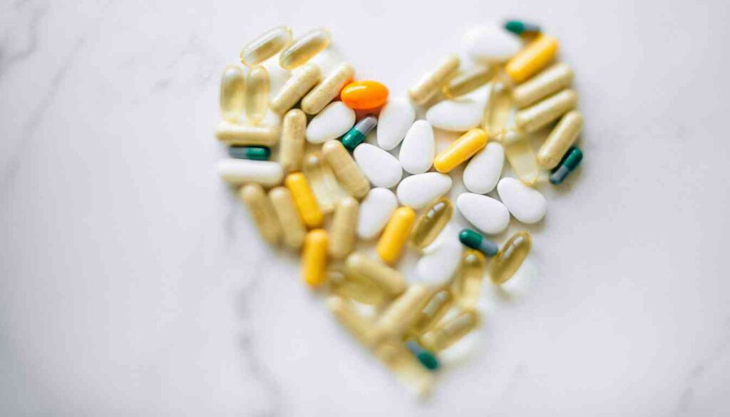 Various pills and capsules arranged in the shape of a heart on a white surface.