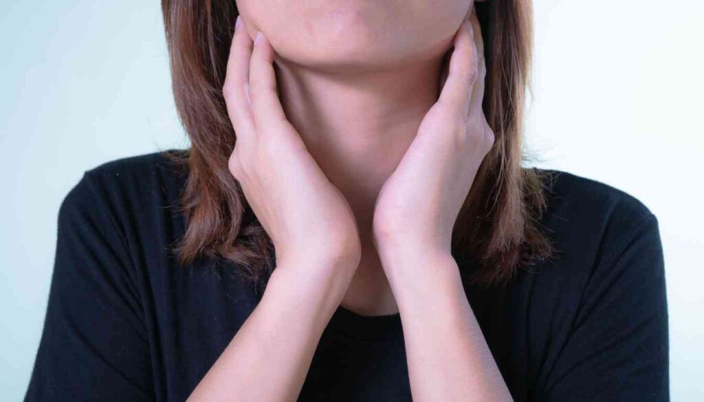 A person with medium-length hair is holding their neck with both hands, indicating possible throat discomfort.