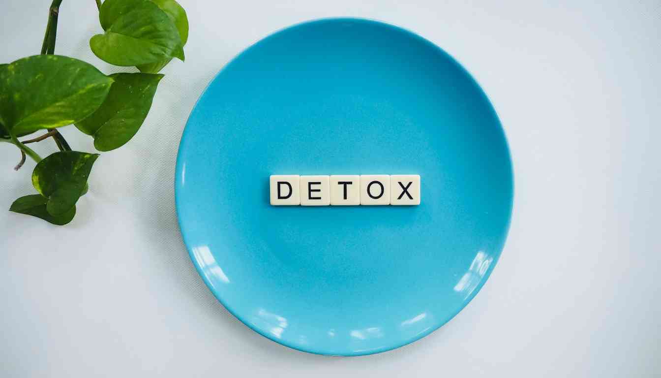 A bright blue plate with the word "DETOX" spelled out in letter tiles, and green plant leaves visible in the corner.