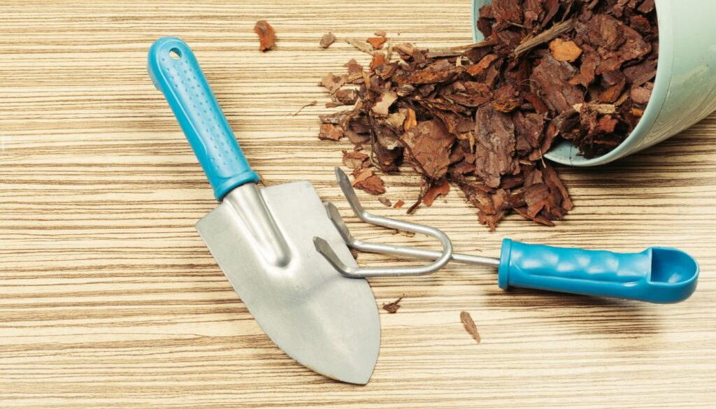 Gardening tools and spilled wood chips on a wooden surface, illustrating materials used for composting.
