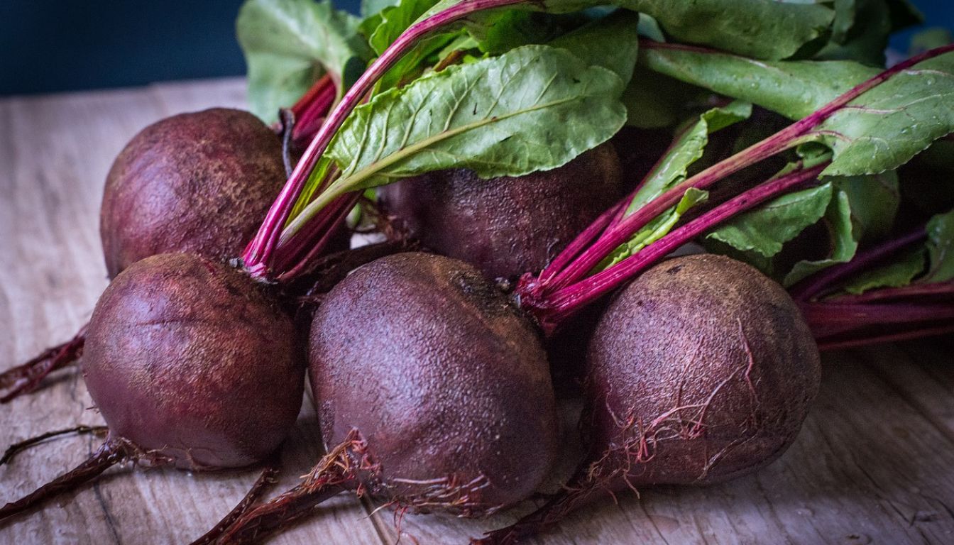 Fresh beets with green leaves attached, lying on a wooden surface.