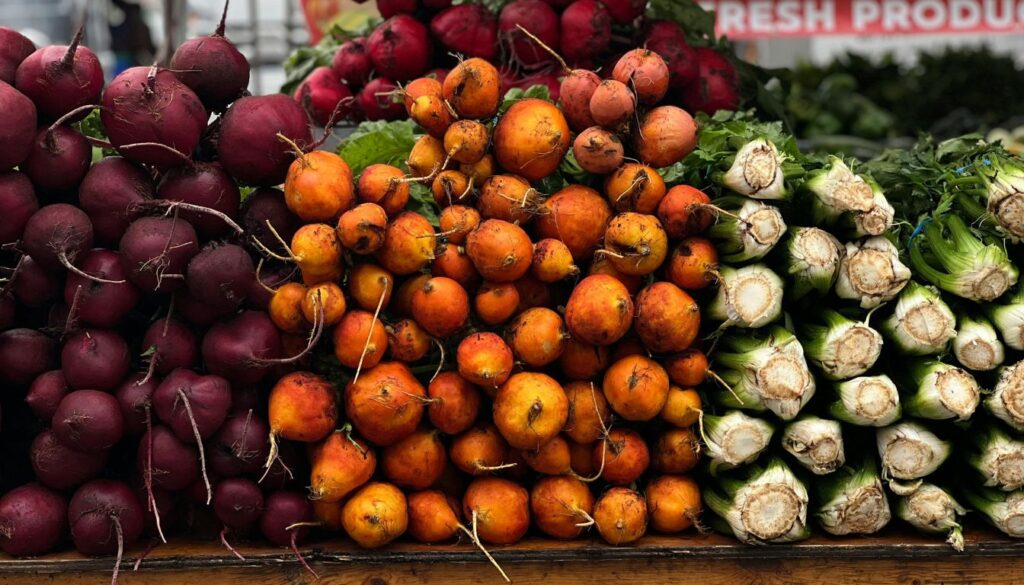 A bunch of vibrant red beets with their green leafy tops, freshly harvested and displayed on a rustic wooden surface.