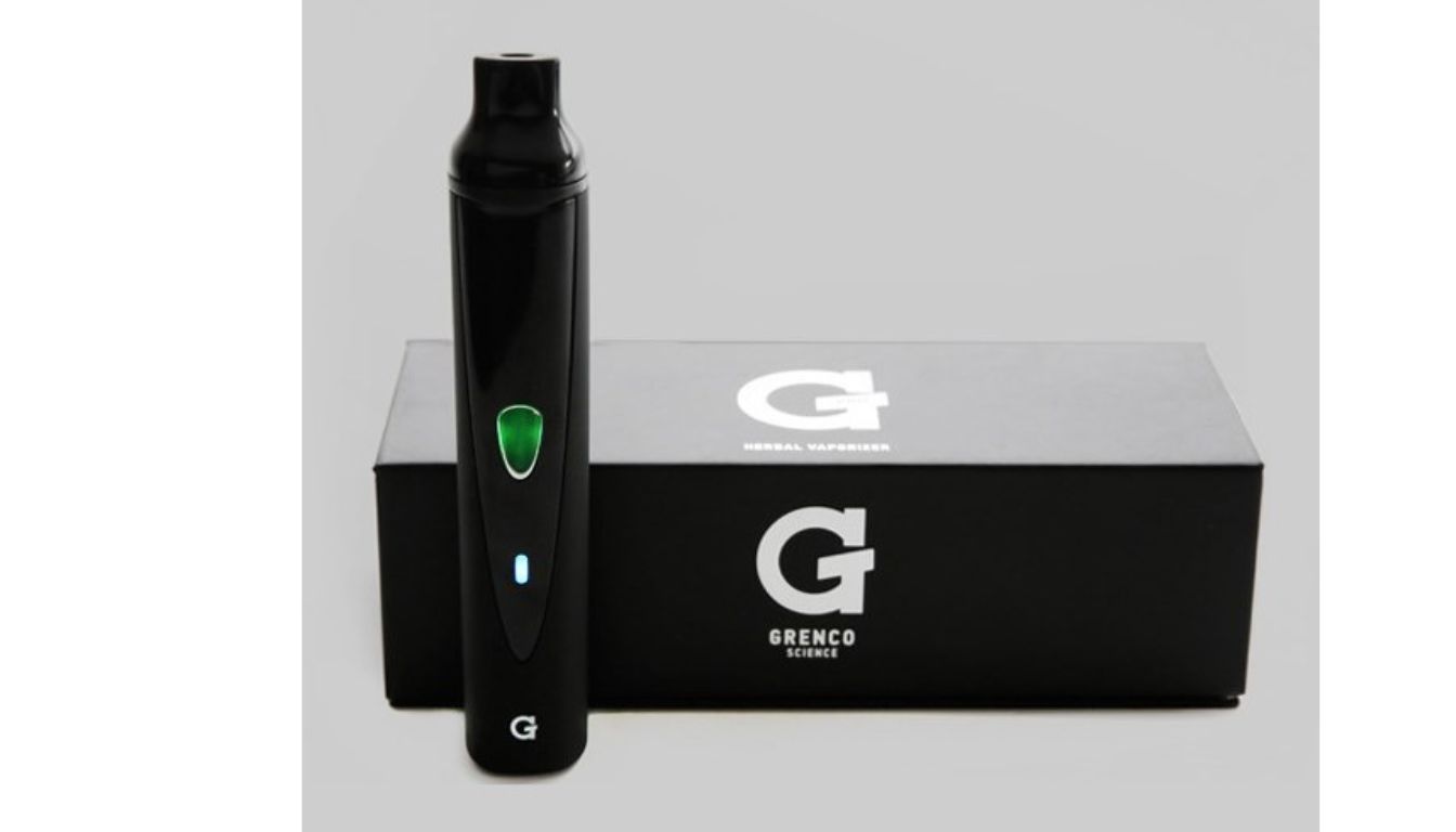 A black Grenco Science herbal vaporizer standing upright in front of its black packaging box. The vaporizer has a green light indicator and a small blue light near the bottom.