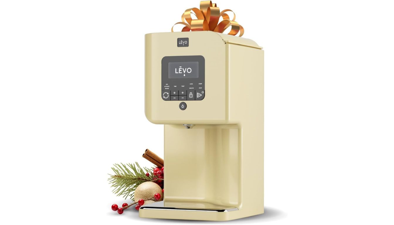 A beige herbal extraction machine with a digital display and control buttons, adorned with a golden ribbon on top, and festive decorations including pine branches, red berries, and a gold ornament at the base.