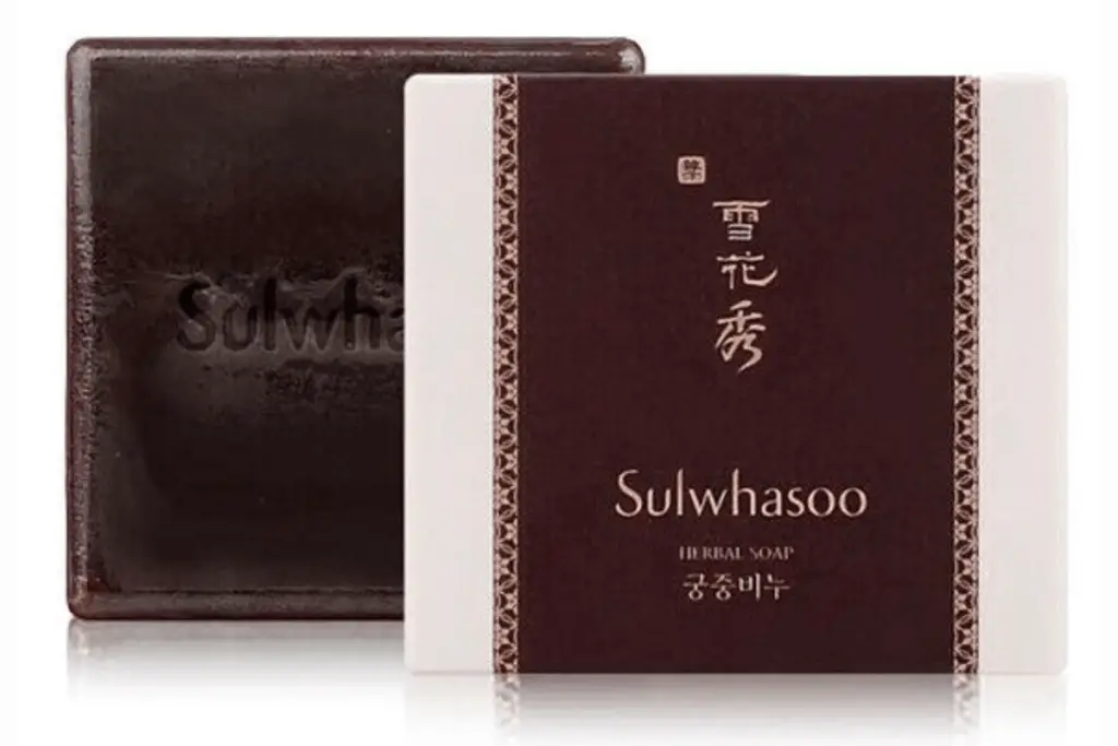 A hand reaches for a box of Sulwhasoo herbal soap on a store shelf, with a price tag and product information displayed nearby