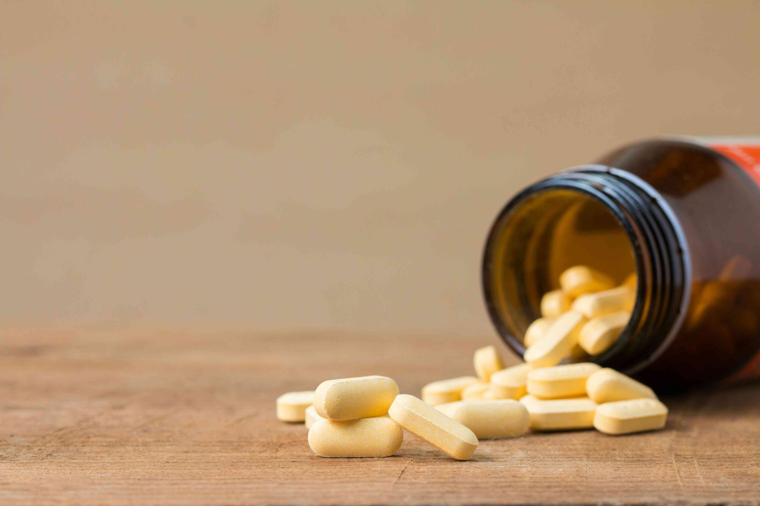 A brown bottle of yellow tablets spilled onto a wooden surface.