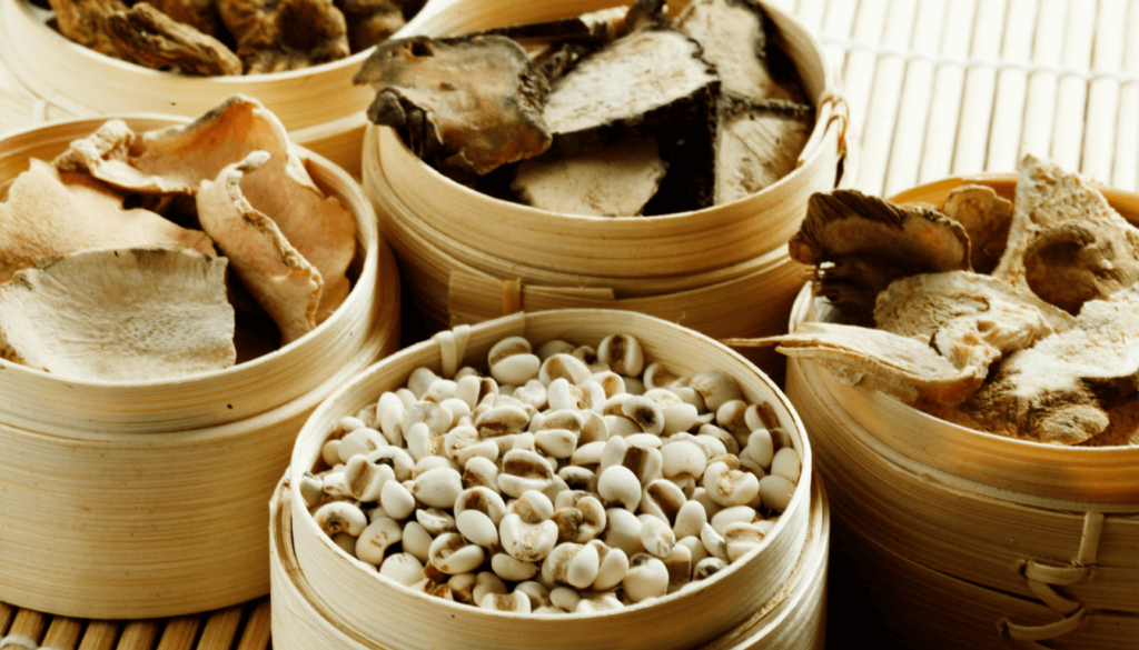 Various traditional Chinese herbal medicines displayed in bamboo containers on a woven mat.