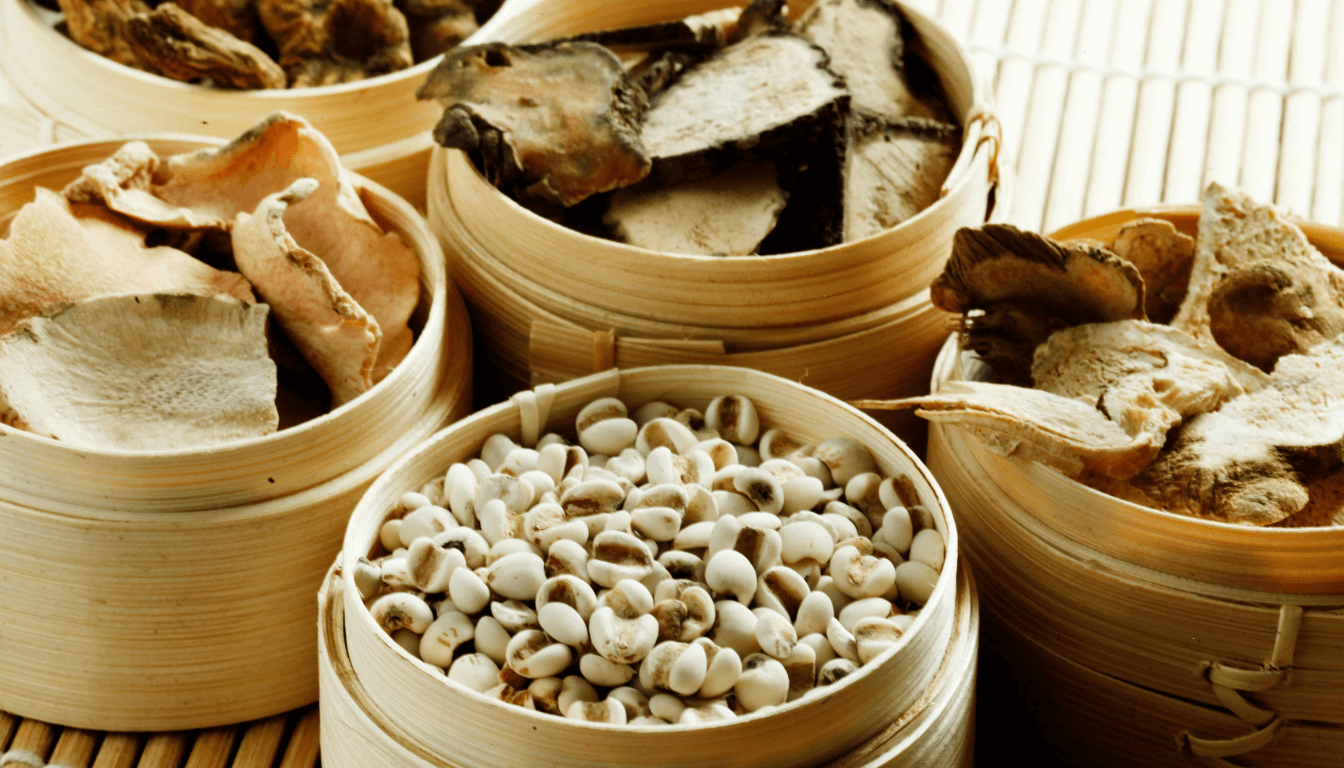 Various traditional Chinese herbal medicines displayed in bamboo containers on a woven mat.