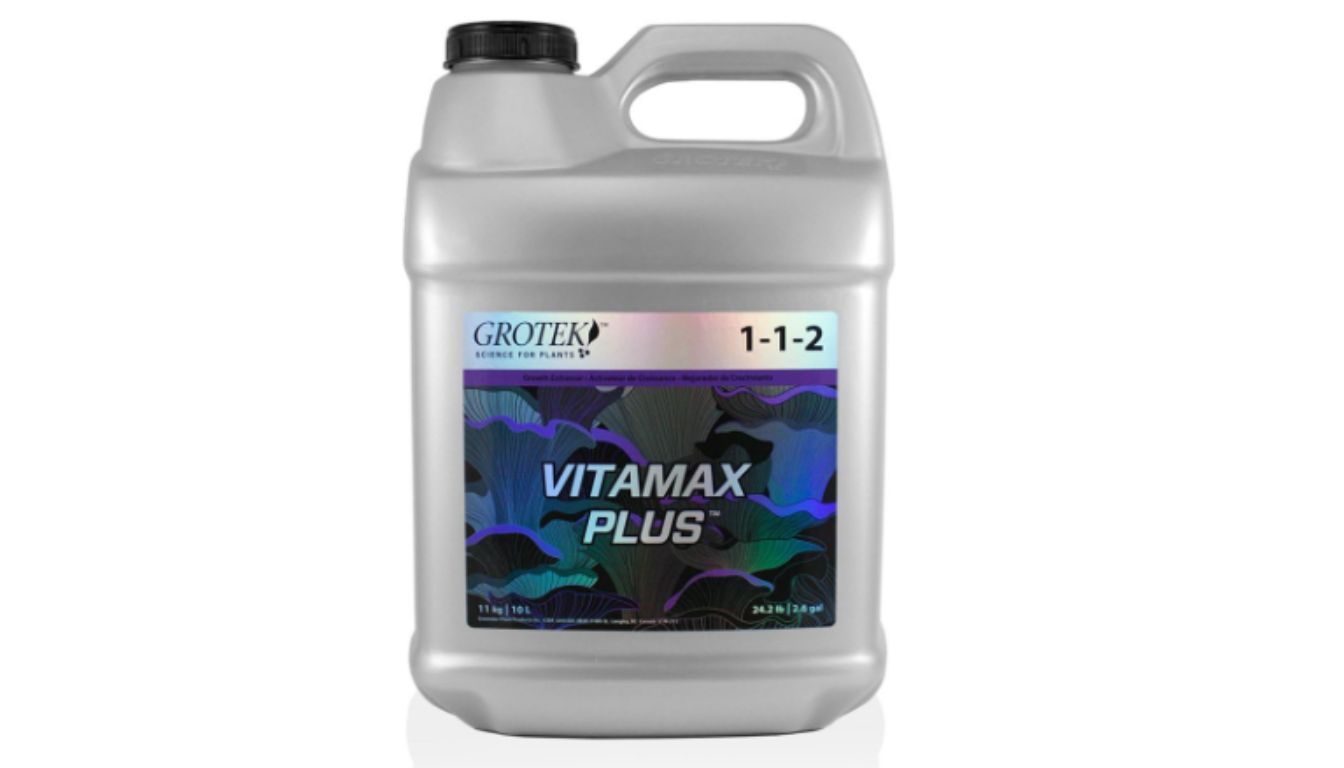 A bottle of Vitamax Plus nutrient solution placed next to healthy, green hydroponic plants.