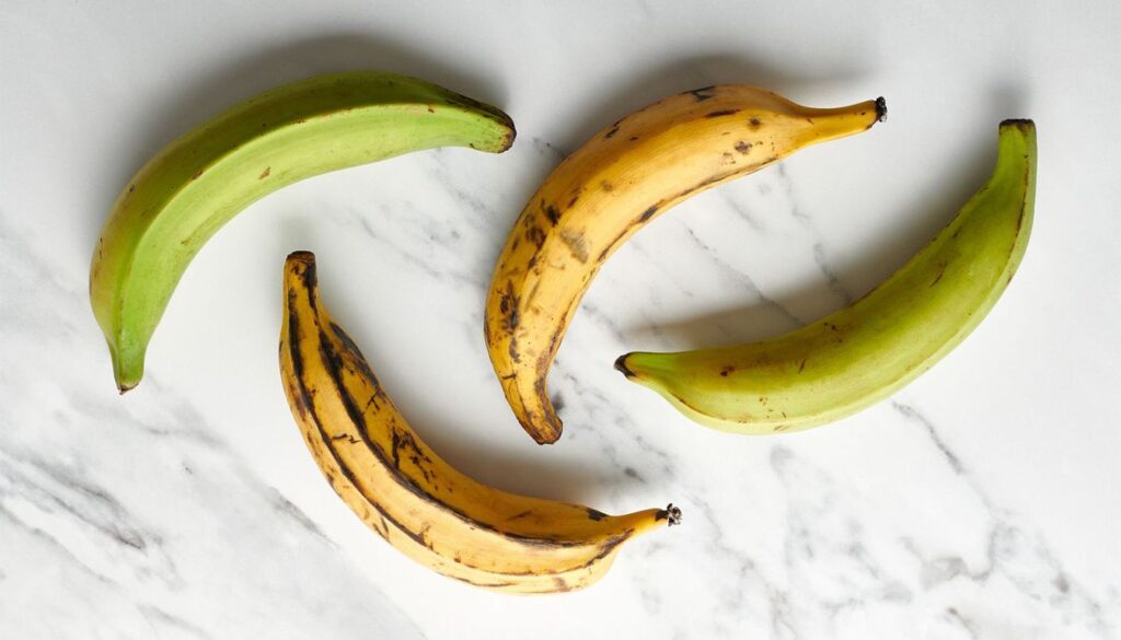 4 Plaintain bananas over a marble table. 2 ripe an 2 not ripe.