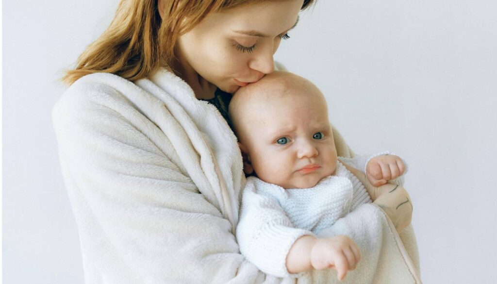 A person wearing a white robe is holding a baby dressed in a white knitted outfit.