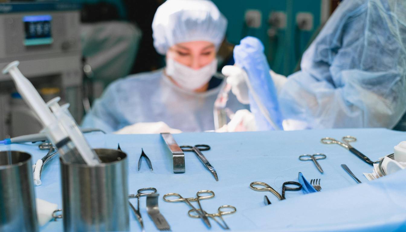 Surgical instruments arranged on a table in an operating room with medical professionals in the background.