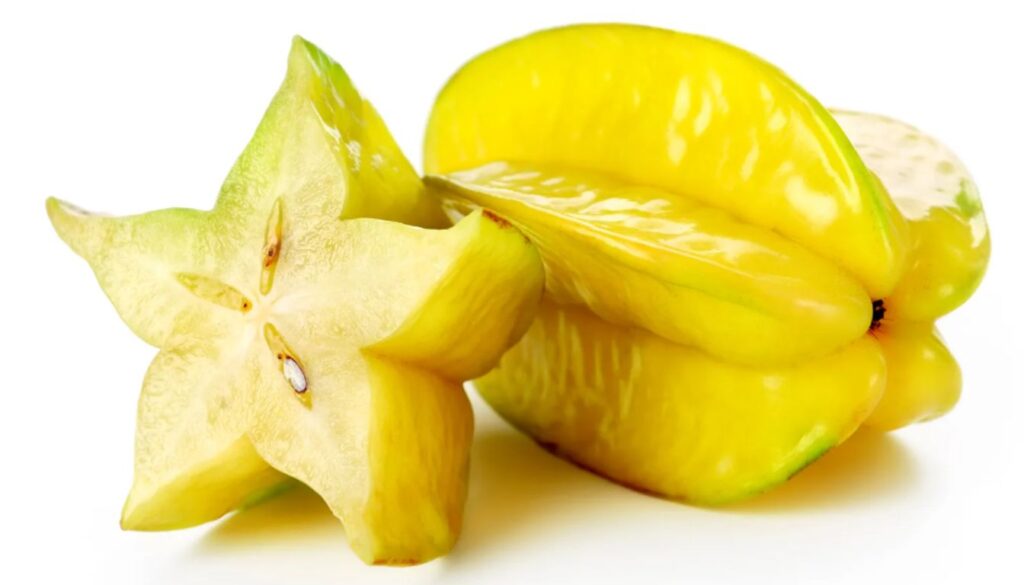 A ripe carambola fruit, also known as starfruit, with one whole and one sliced piece revealing the star-shaped cross-section, on a white background.