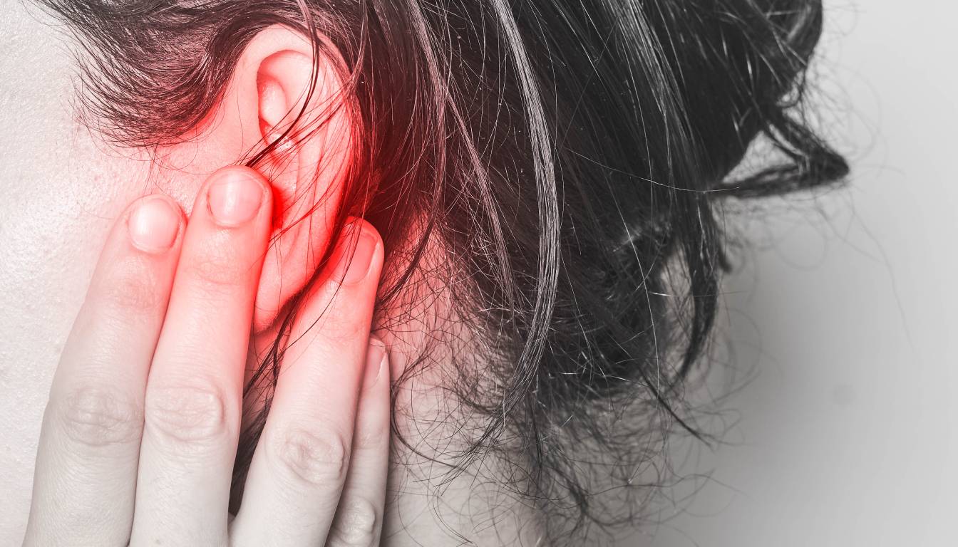 A person holding their ear with their hand, with a red glow indicating pain or discomfort around the ear area.