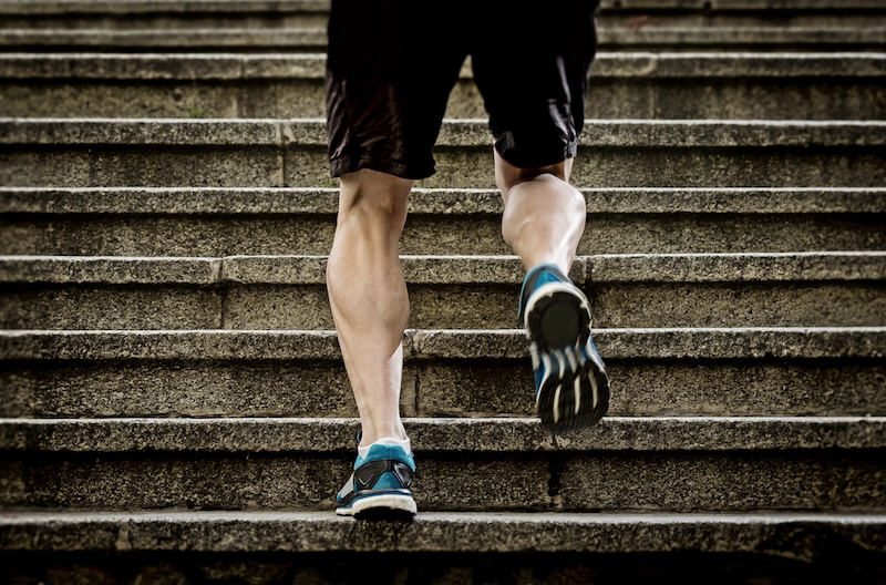 A person running up a set of stone stairs, wearing black shorts and blue running shoes.